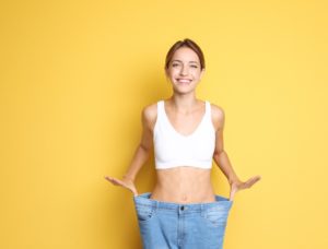 ダイエットに成功した女性が笑顔でウエストがゆるくなったジーンズをはいている